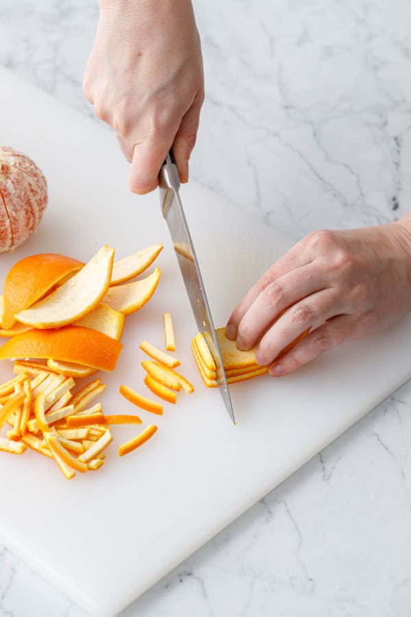 Cutting a stack of orange peel wedges into 1/4-inch thick slices.