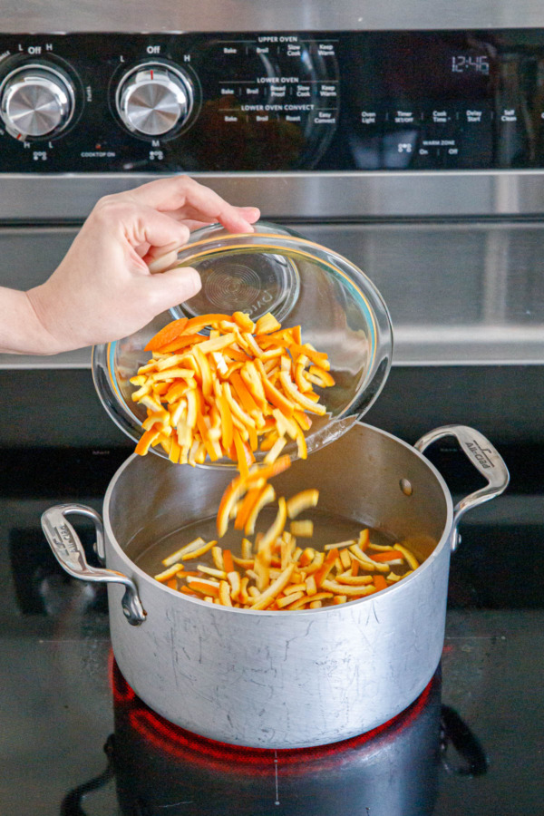 Pouring cut slices of orange peel into saucepan with sugar syrup.