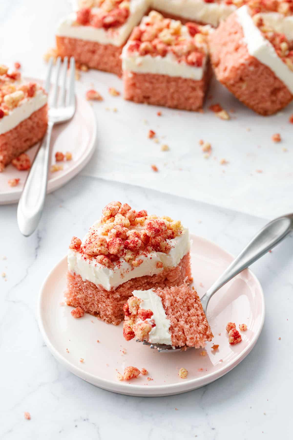 Cut piece of Strawberry Crunch Sheet Cake with Buttermilk Frosting on a pink dessert plate with a bite sitting on the fork on the side.