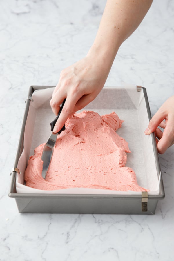 Offset spatula spreading pink cake batter into 13x9 cake pan.