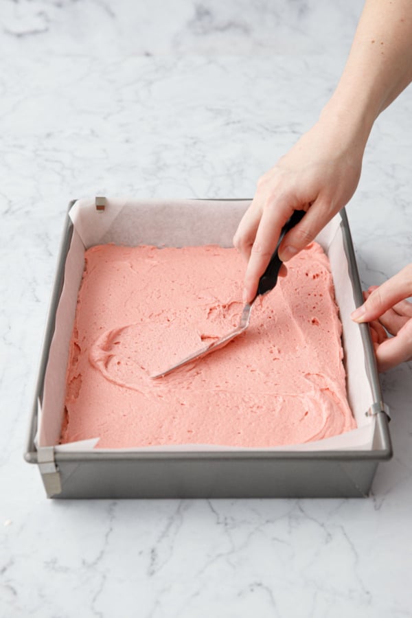 Offset spatula spreading cake batter into an even layer in baking pan.