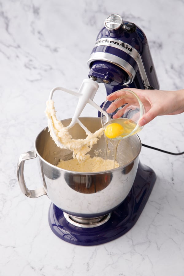 Adding eggs to stand mixer bowl with creamed butter and sugar.