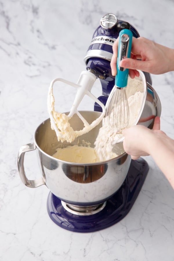 Pouring dry flour ingredients into mixing bowl with butter, sugar, and egg mixture.