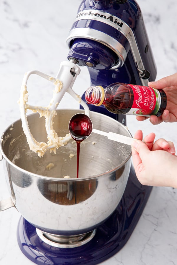 Pouring Amoretti Strawberry Artisan flavoring into stand mixer bowl with cake batter.