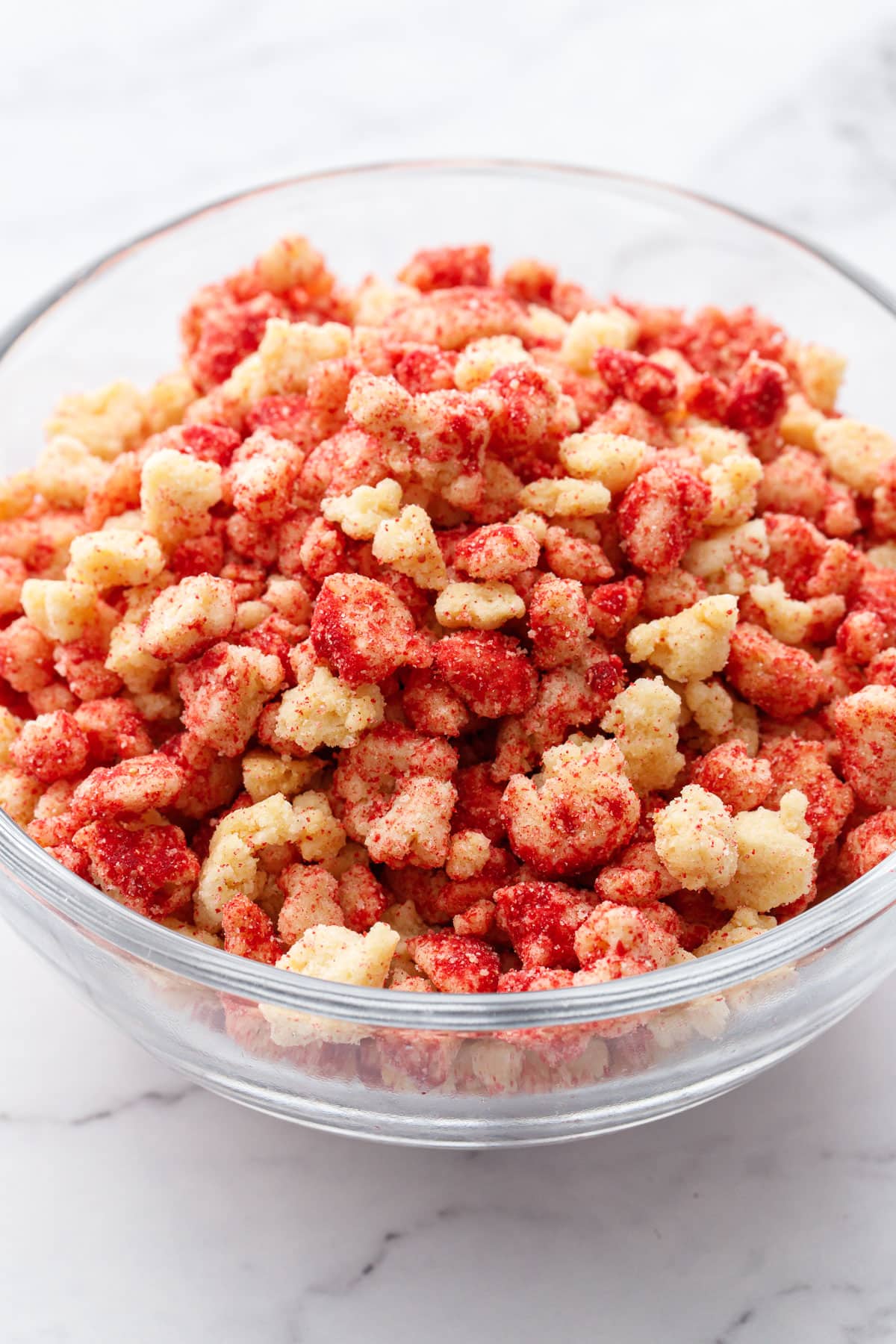 Closeup, glass bowl filled with dual-colored Strawberry Shortcake Crunch Topping on a marble background.