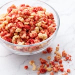 Glass bowl of Strawberry Shortcake Crunch Topping on a marble background, with a few crumbs scattered alongside the bowl.