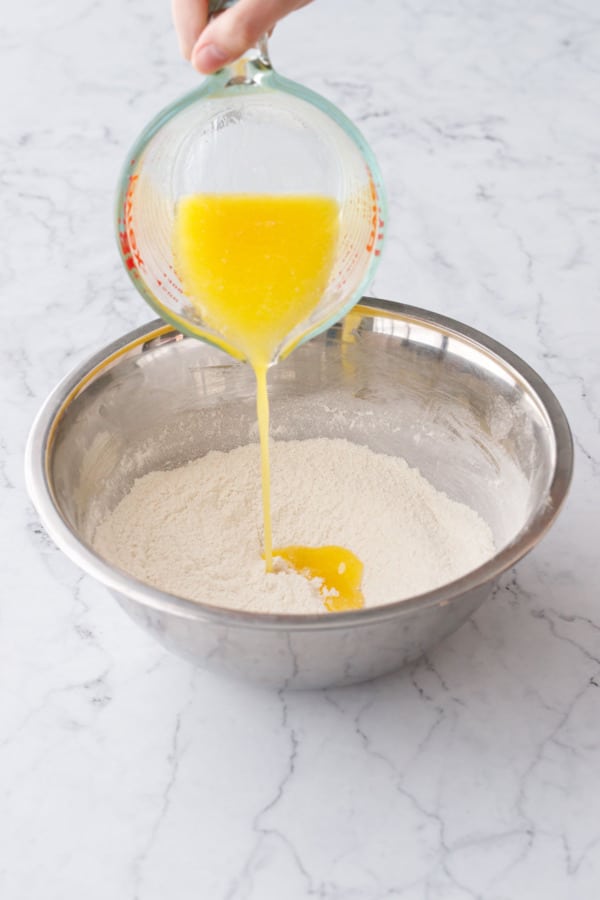 Pouring melted butter into metal mixing bowl along with other dry ingredients.