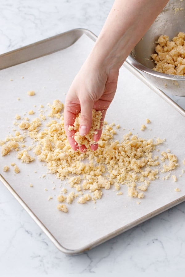 Crumbling shortcake crumb dough onto a parchment lined cookie sheet.
