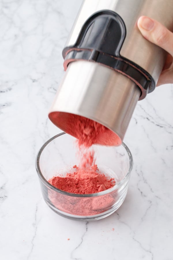 Pouring ground strawberry powder from coffee grinder into a small bowl.