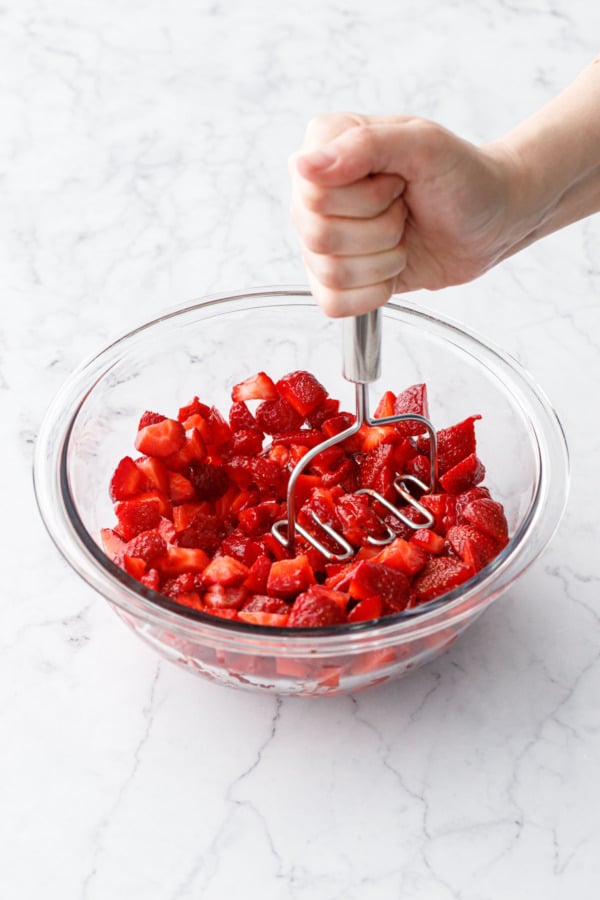 Mashing chopped ripe strawberries with a potato masher.