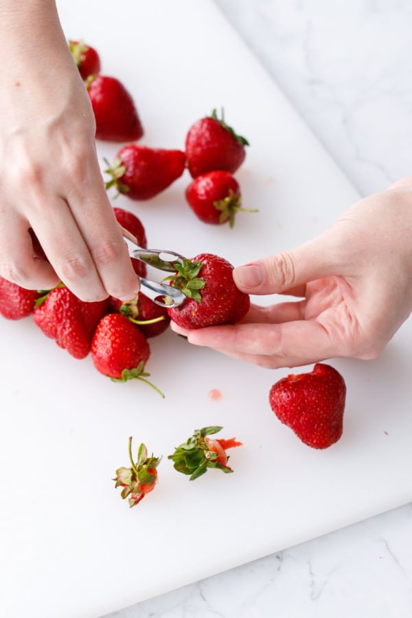 Using a strawberry huller to remove hulls from fresh strawberries.