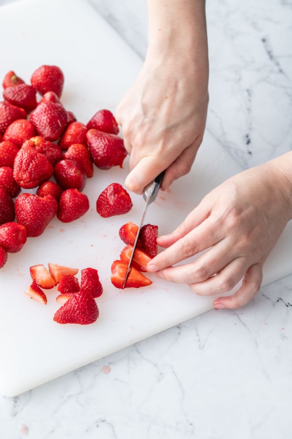 Chopping fresh hulled strawberries on a white cutting board.