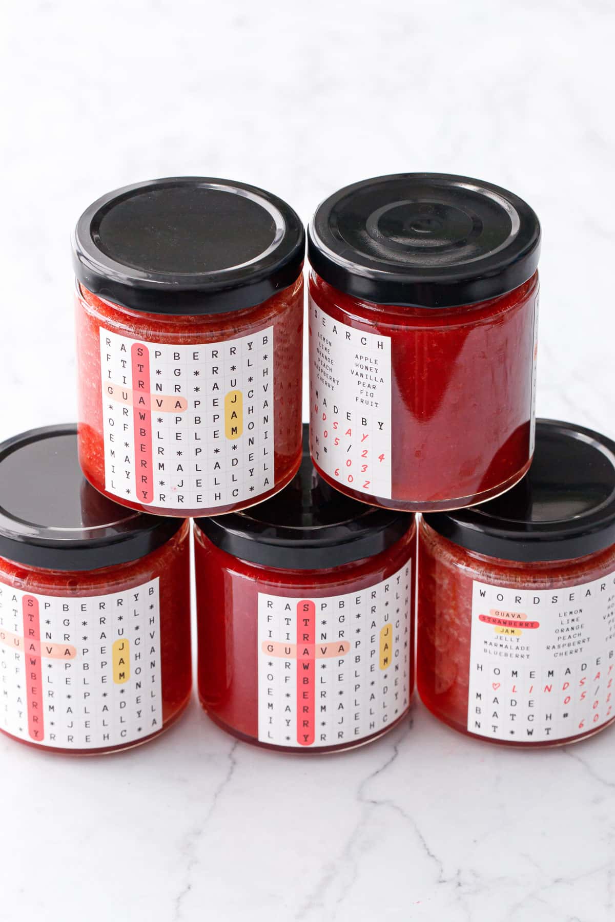 Stack of Guava Strawberry Jam in jars with black lids and crossword puzzle labels.