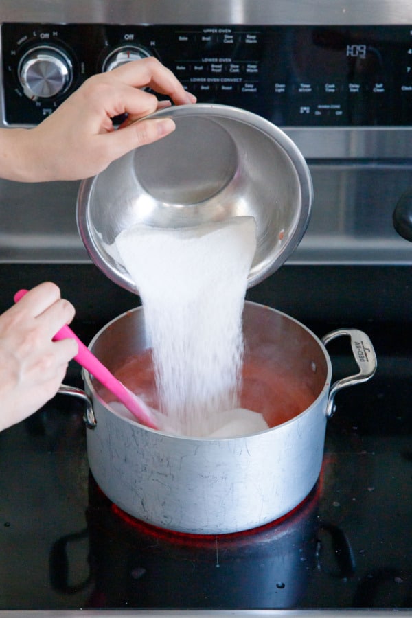 Pouring sugar-pectin mixture into saucepan with boiling fruit.