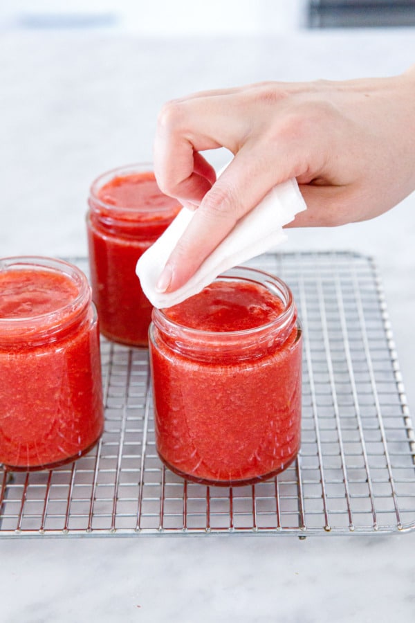 Wiping the rims of the filled jam jars with a wet paper towel.