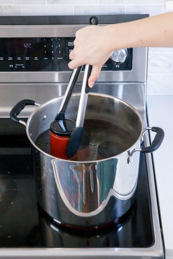 Lowering filled jam jars into a large canning pot filled with nearly-boiling water.