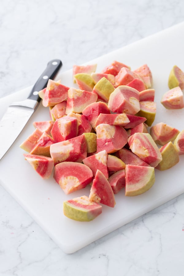 Chopped pink guava on a white cutting board with knife.