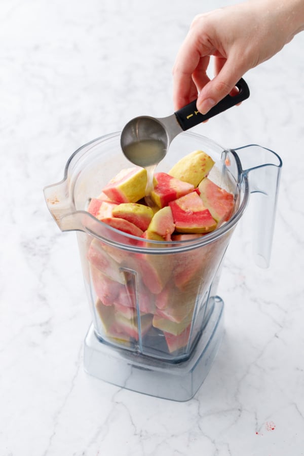 Adding lemon juice to a blender canister filled with coarsely chopped pink guava.