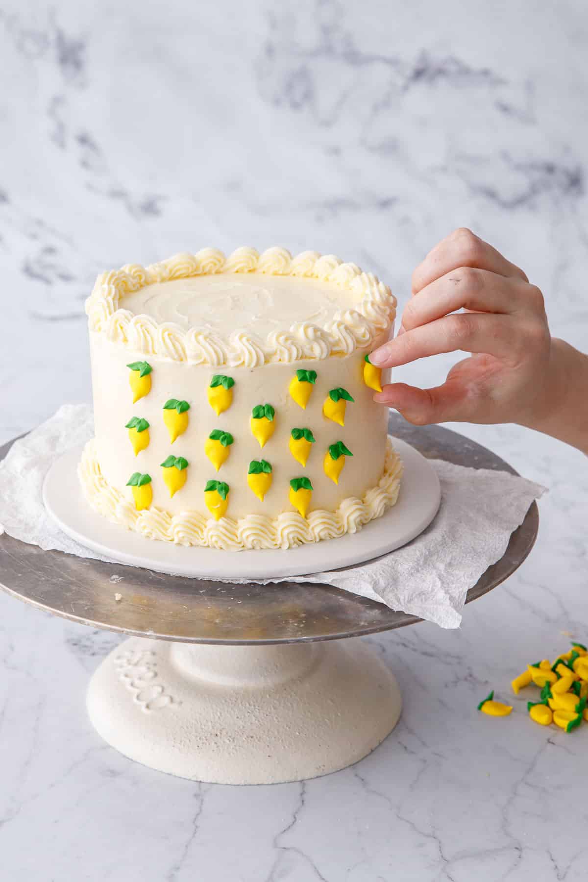 Placing small royal icing lemons on the side of the frosted cake for decoration.