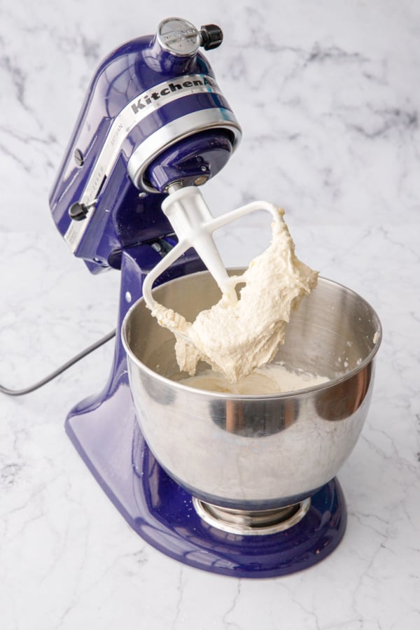 Mixer with beater lifted showing the consistency of the cake batter after mixing in lemon juice and half of milk.