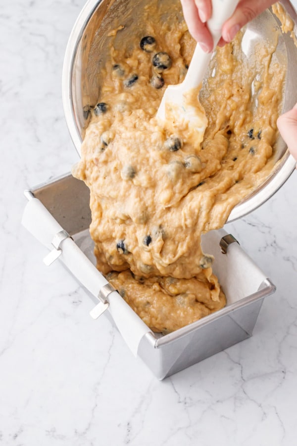 Pouring blueberry banana bread batter into a parchment-lined loaf pan.