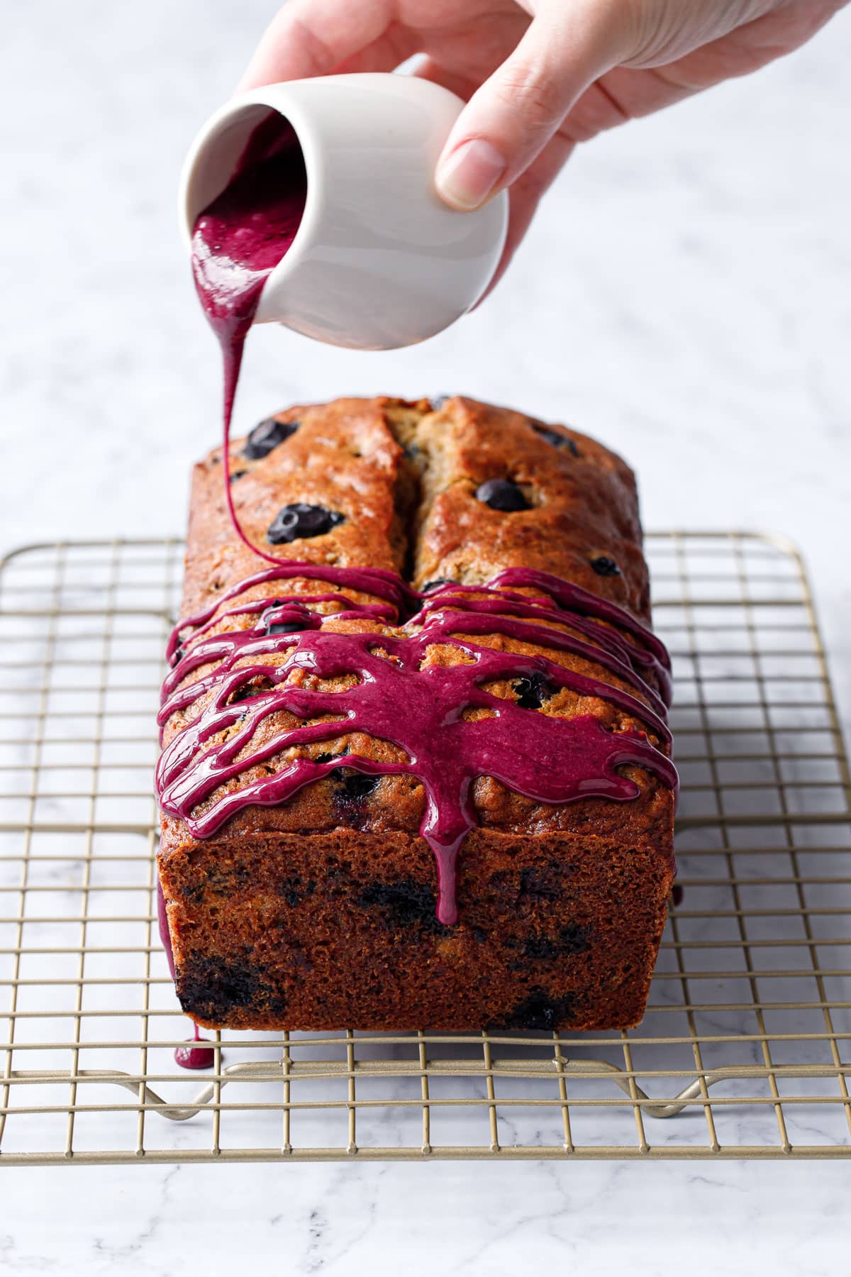 Drizzling Blueberry Banana Bread with a bright magenta blueberry glaze, with a distinct drip coming off the front.