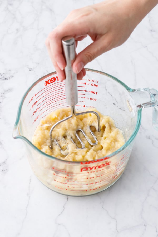 Mashing ripe bananas in a 4 cup glass measuring cup with a wire potato masher.