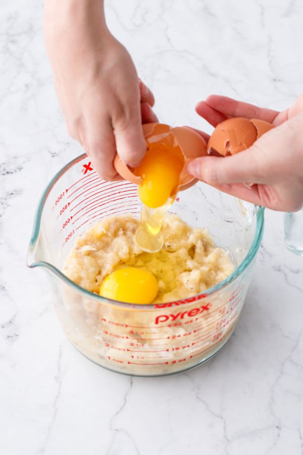 Cracking two eggs into measuring cup along with mashed banana.
