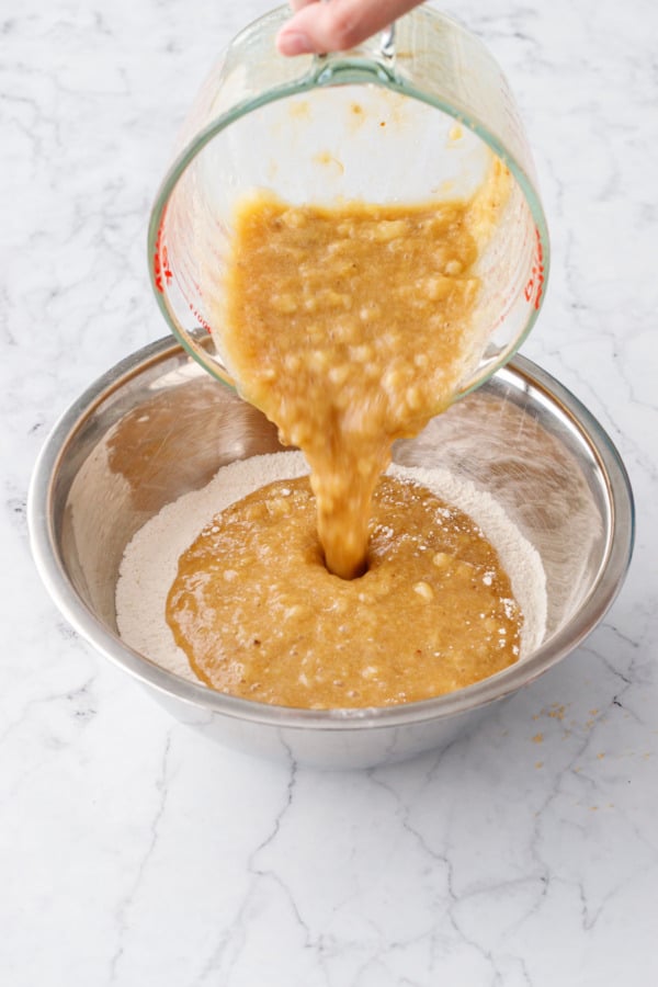 Pouring combined wet ingredients into metal mixing bowl with dry ingredients.