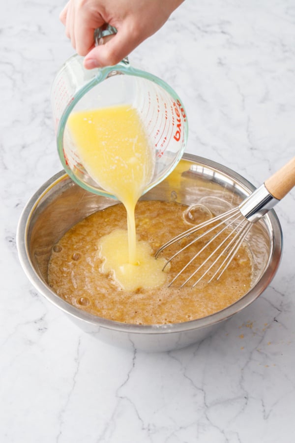 Pouring lukewarm melted butter into mixing bowl along with other wet ingredients.