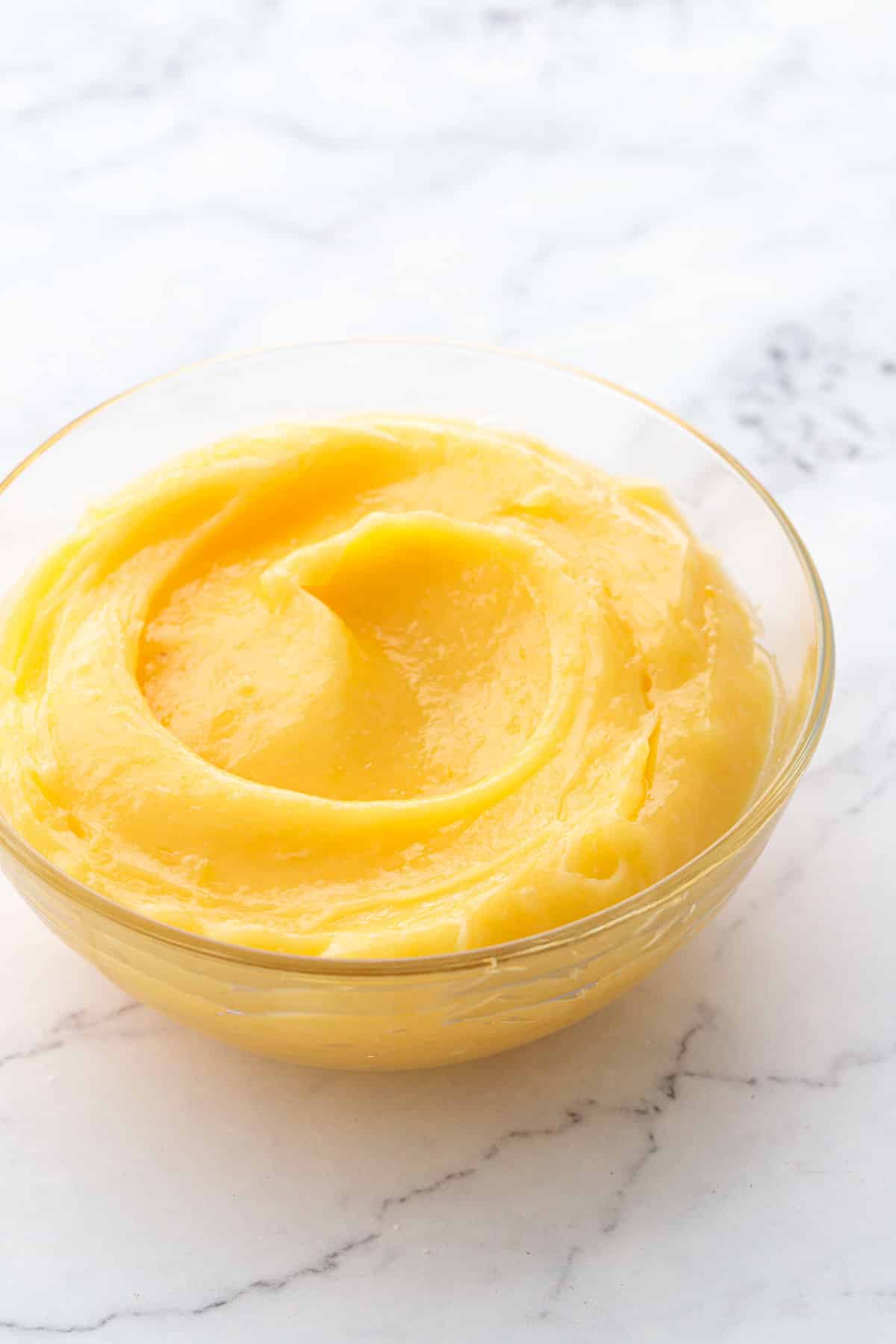 Glass bowl with a swirl of Meyer lemon curd on a marble background.
