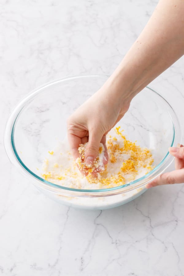 Rubbing lemon zest into granulated sugar in a glass mixing bowl.