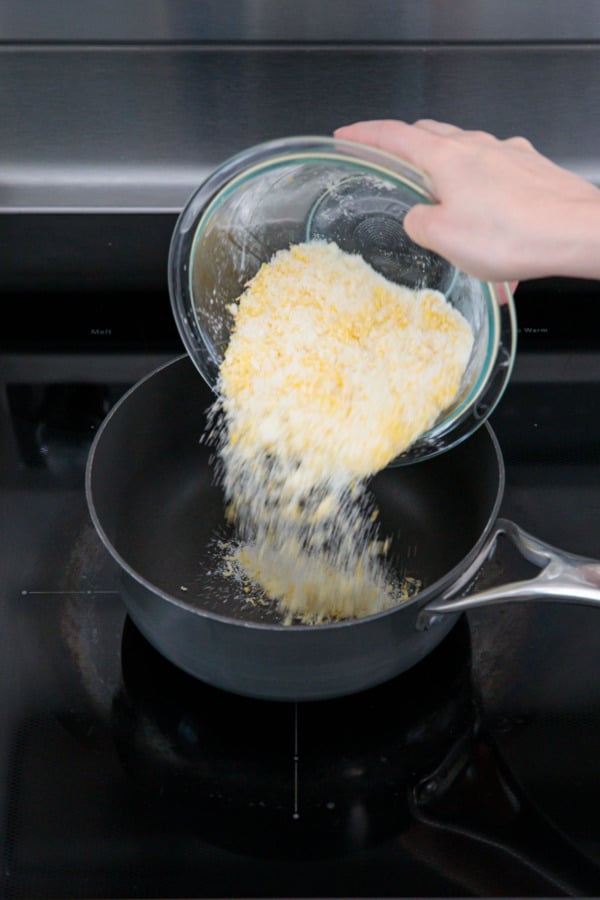 Pouring lemon zest-infused sugar into a saucepan on the stove.