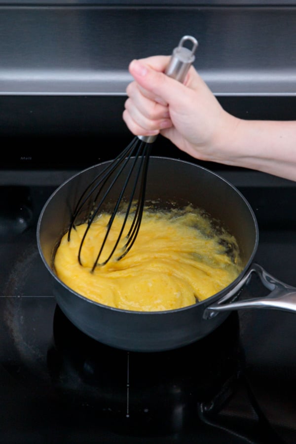Whisking eggs into sugar mixture in a saucepan on the stove.