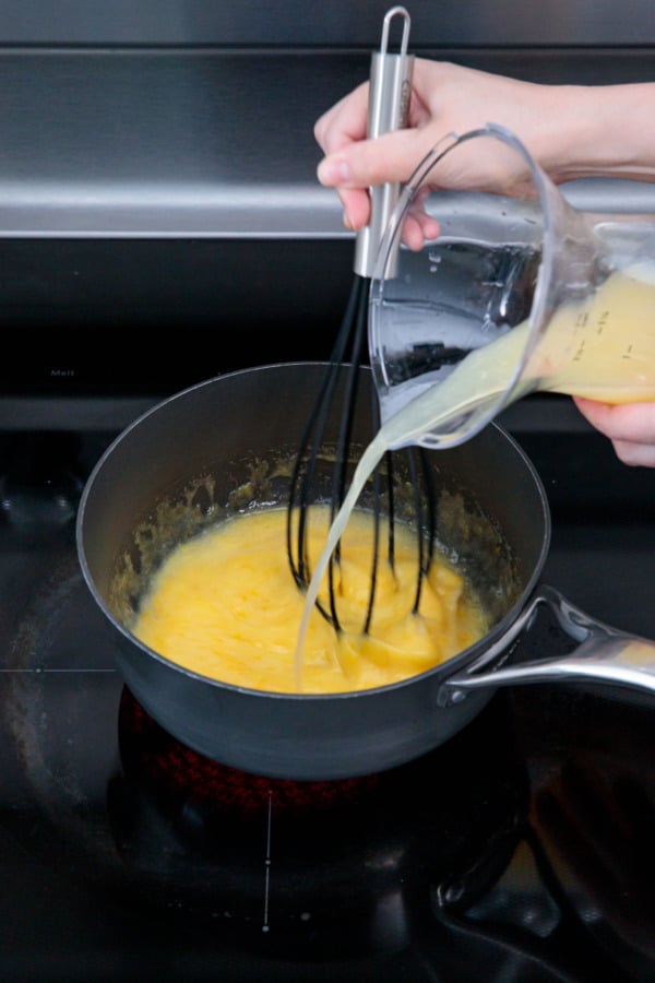 Slowly pouring in lemon juice into saucepan with egg and sugar mixture while whisking.