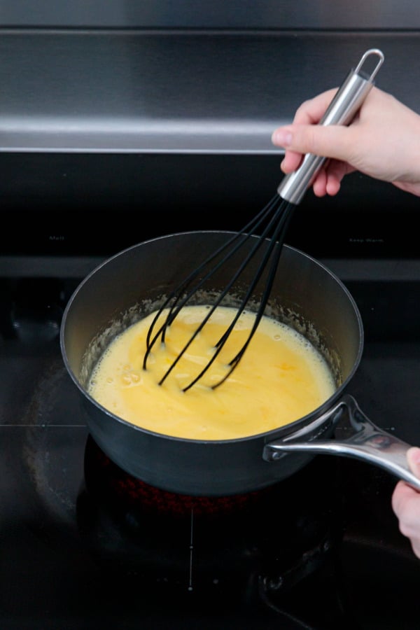 Whisking the thin curd mixture in a saucepan on the stovetop.