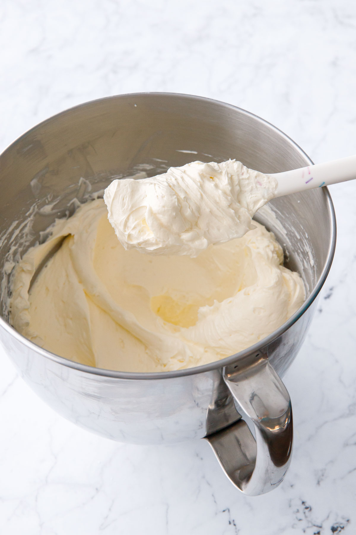 Bowl of Swiss Meringue Buttercream in a metal mixing bowl with white spatula.
