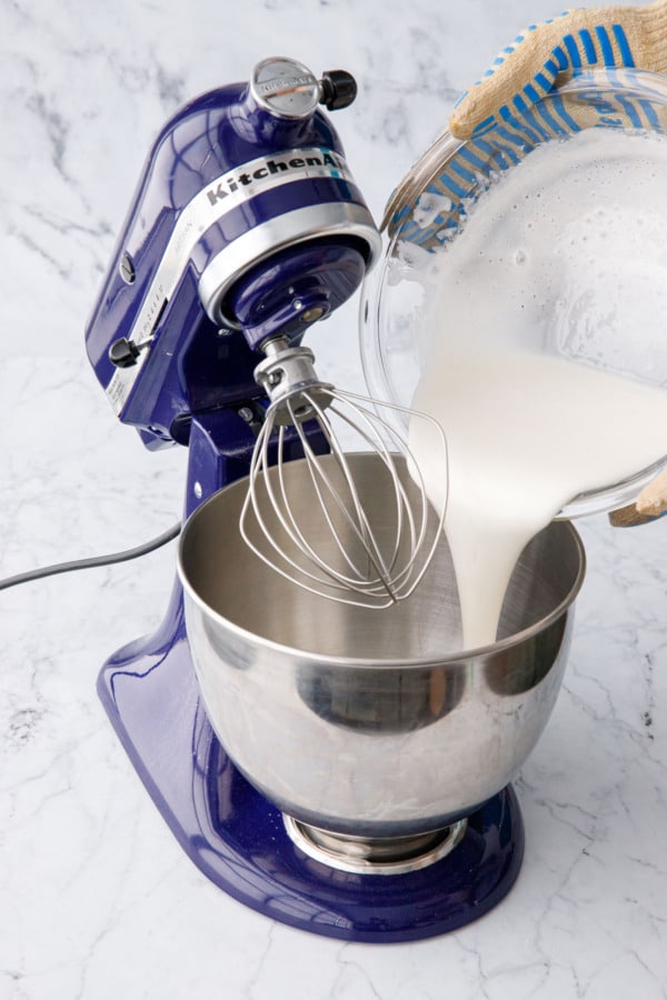Pouring the cooked egg white and sugar mixture into the bowl of a stand mixer.