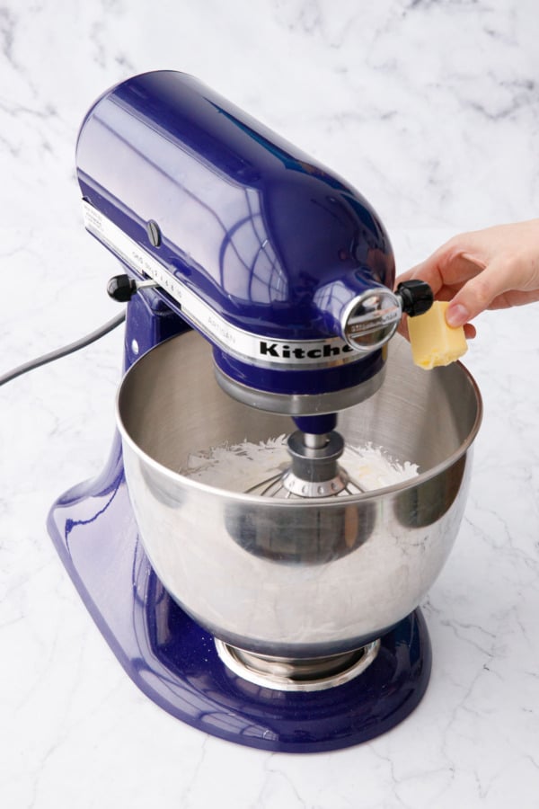Adding butter to the cooled meringue in a stand mixer.