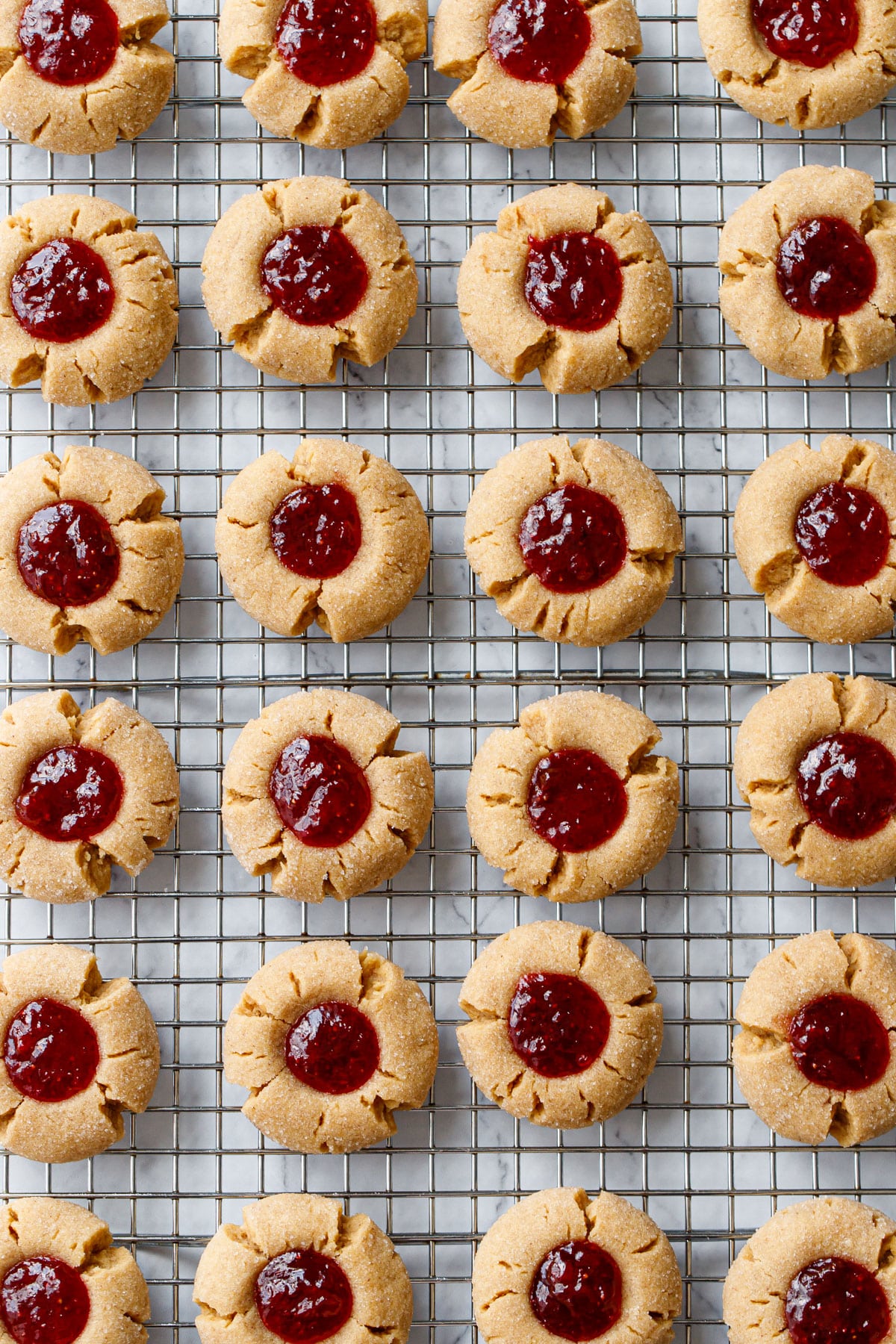 Overhead, neat rows of Peanut Butter & Jam Thumbprints on a wire baking rack.