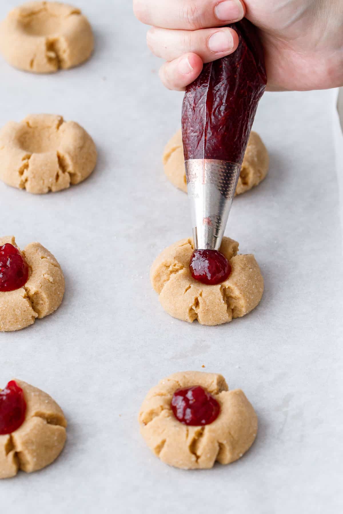 Piping strawberry jam into the thumbprint cavities of partially baked cookies.