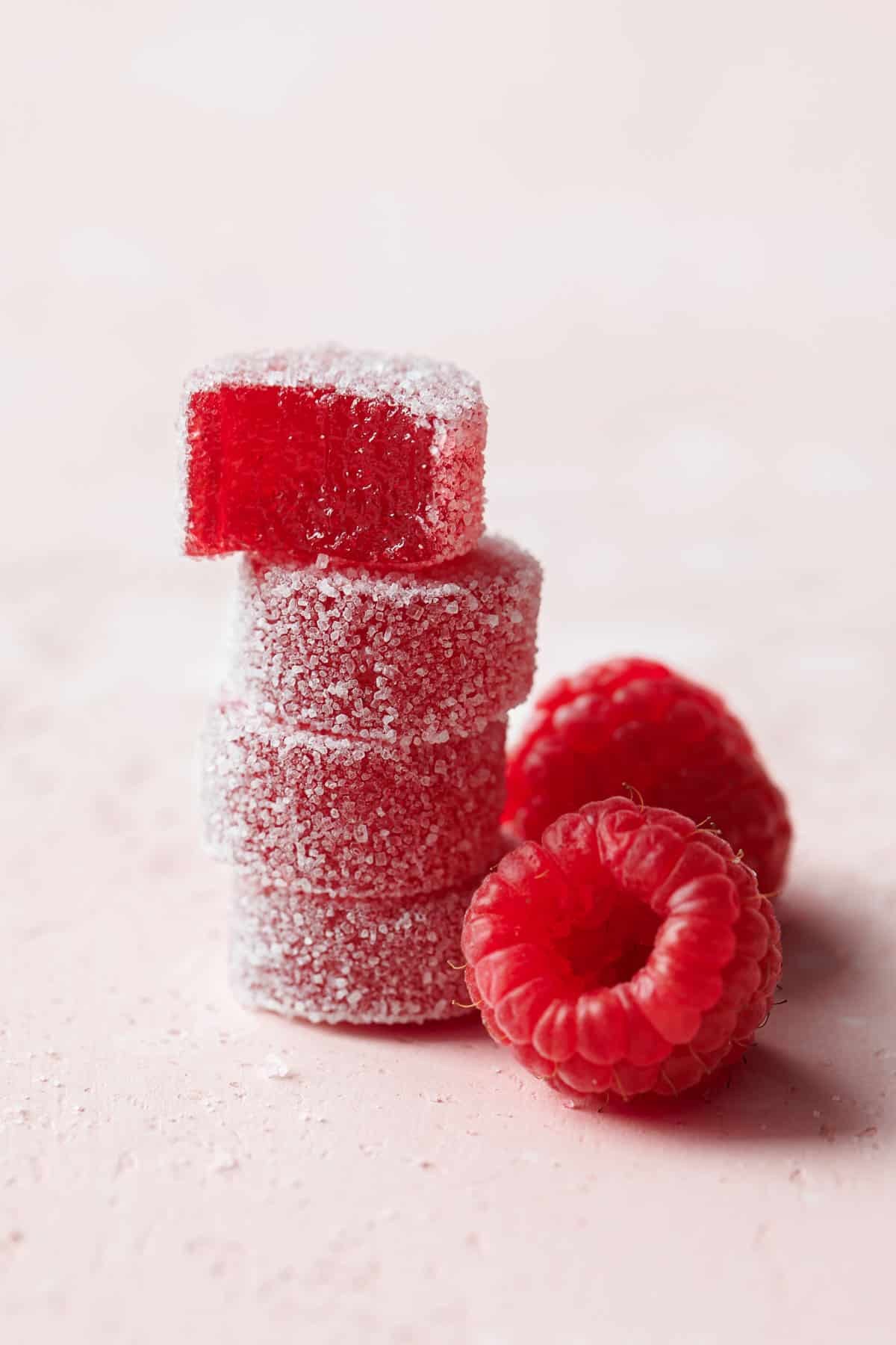 Stack of Homemade Raspberry Pectin Gummies, top one with a bite taken out of it, and two raspberries on the side.