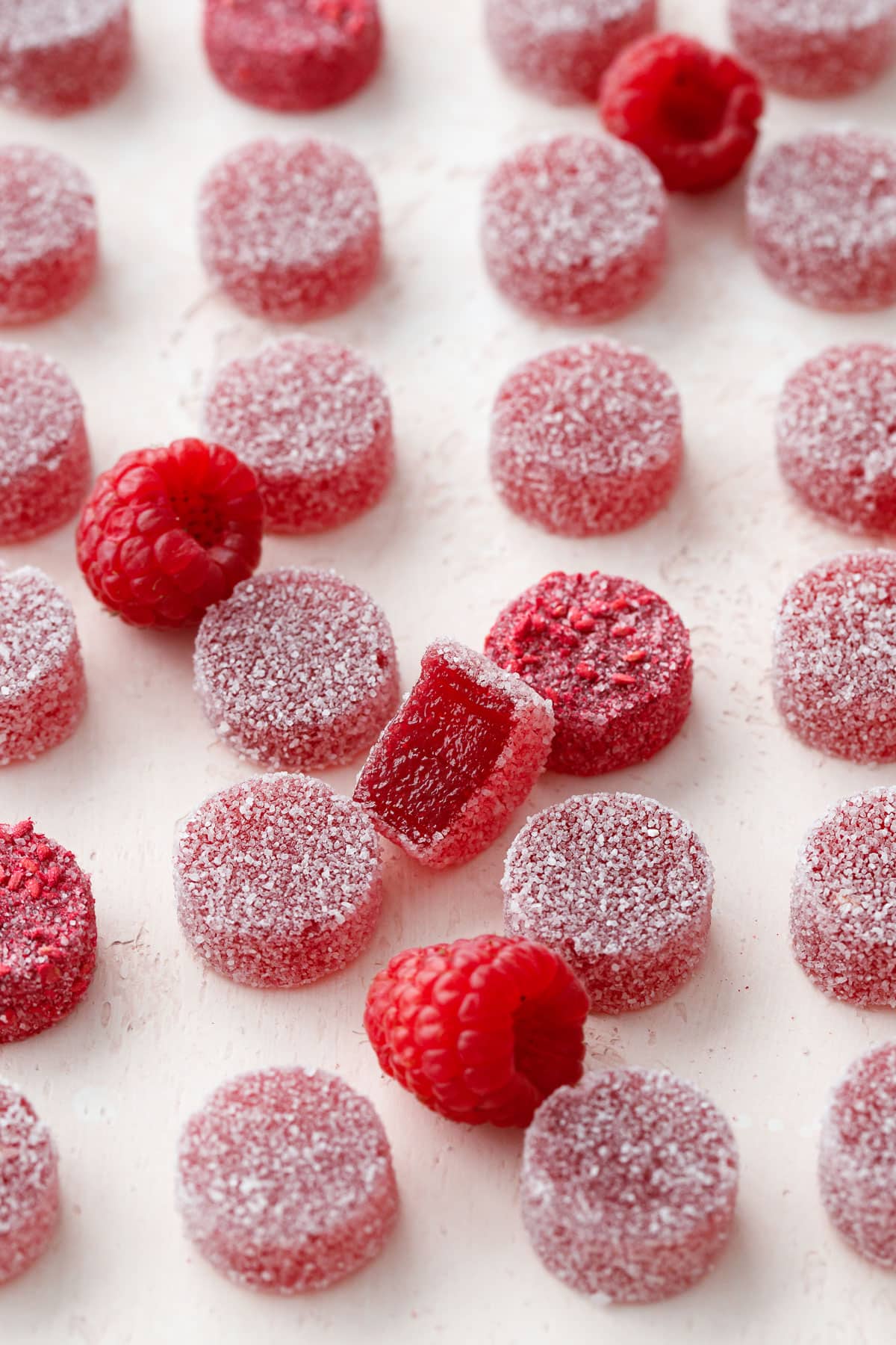 Neat rows of Homemade Raspberry Pectin Gummies with one bitten candy and a few raspberries breaking up the grid.