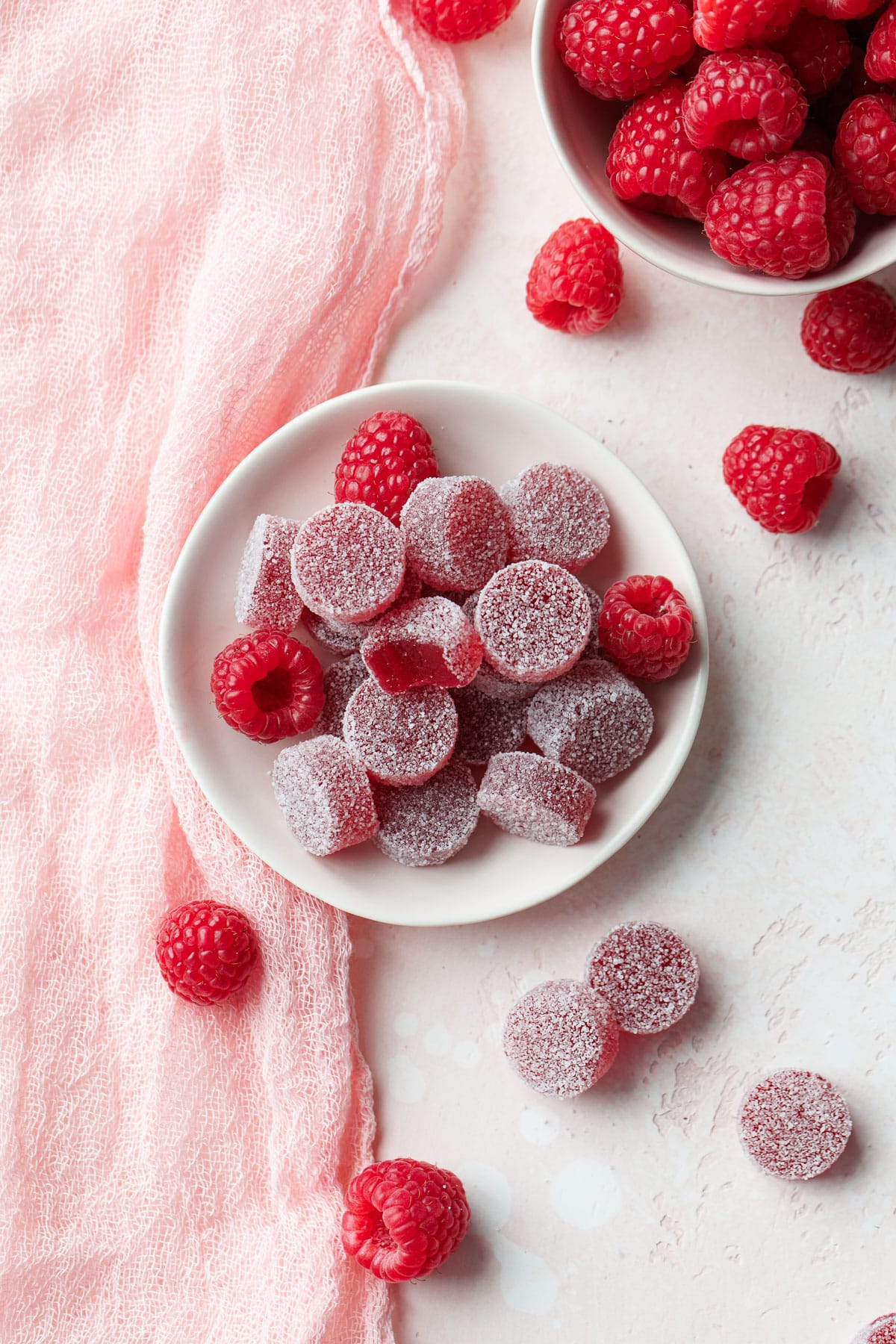 Overhead, small dish of Homemade Raspberry Pectin Gummies with a bowl of raspberries and a few more scattered around.