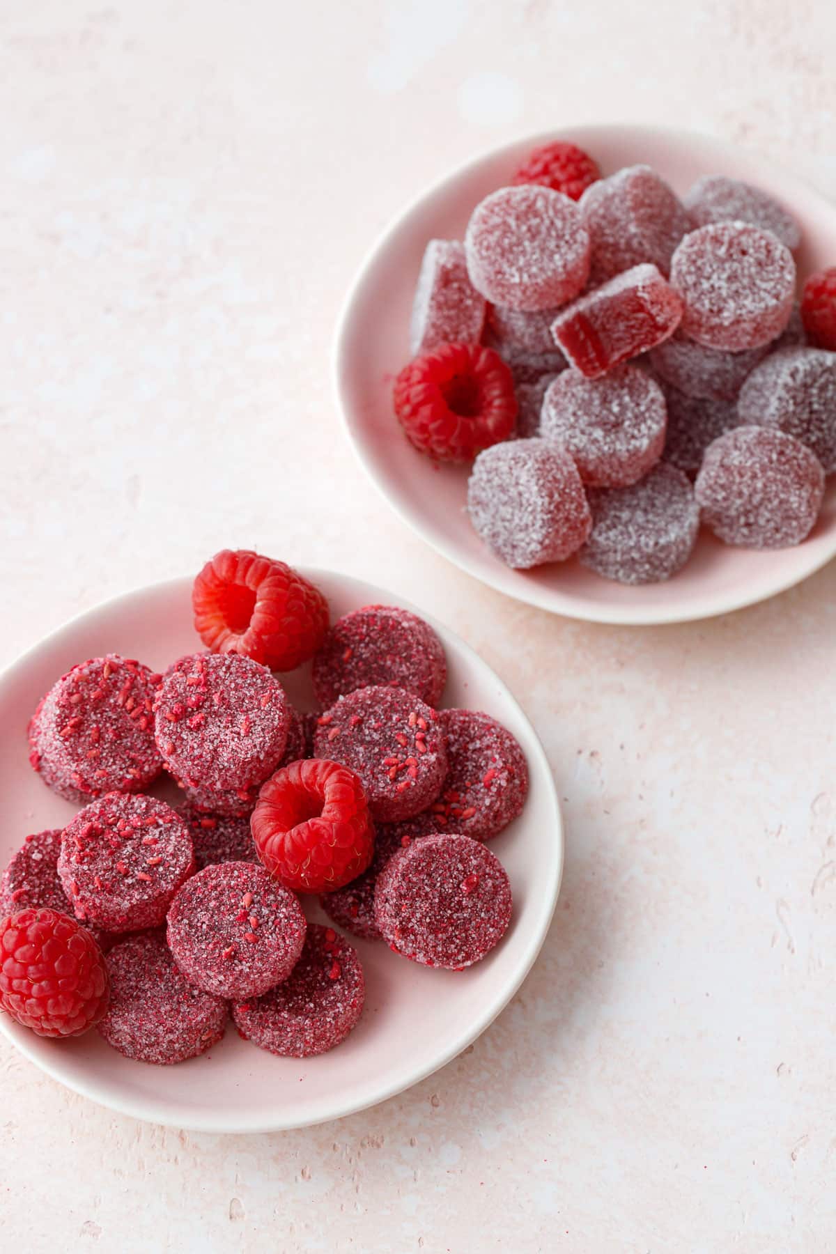 Two dishes of Homemade Raspberry Pectin Gummies with different coatings, one with plain sugar and the other with sugar mixed with freeze dried raspberries.