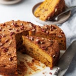 Triangular slices of Pumpkin Pecan Coffee Cake on a marble cake plate, one slice on a plate in the background with a cup of coffee.