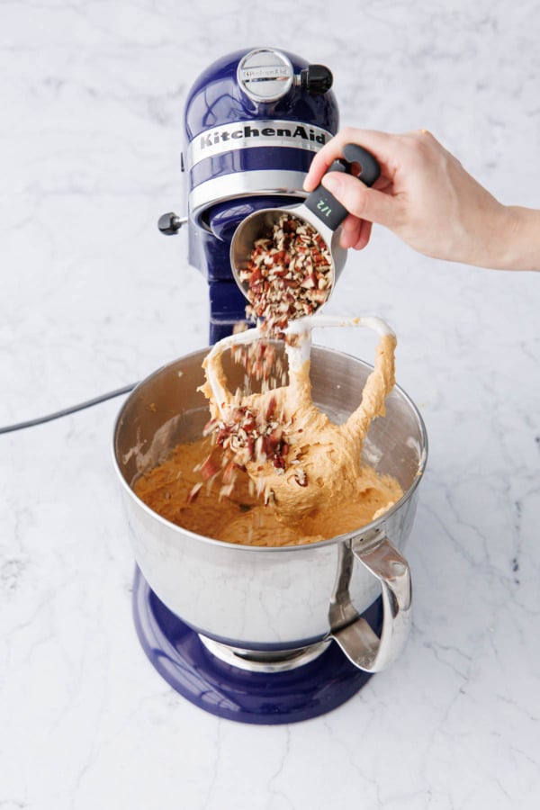 Adding chopped pecans to mixing bowl with pumpkin coffee cake batter.