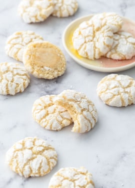 Chewy Lemon Almond Crinkle Cookies scattered on a marble background with a few cookies on a small cookie plate.
