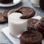 Chewy Chocolate Molasses Cookie with a bite taken out of it resting on top of a glass of milk, more cookies arranged around it.