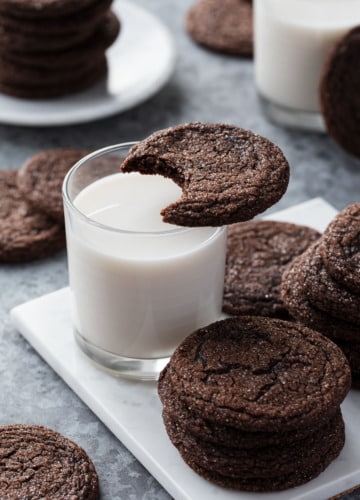 Chewy Chocolate Molasses Cookie with a bite taken out of it resting on top of a glass of milk, more cookies arranged around it.